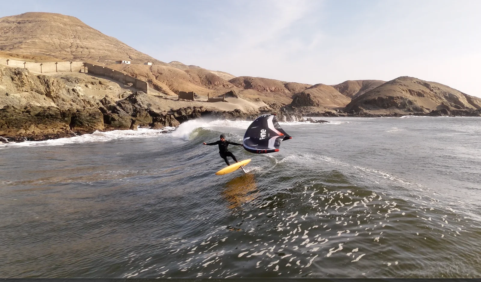 Fernando Mizo wing foiling along a coastal wave.