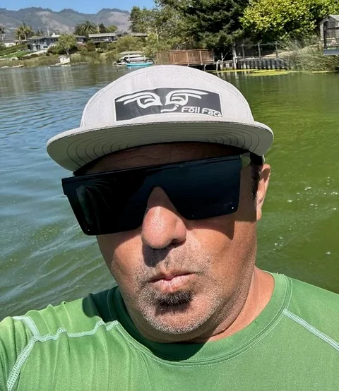 Henry Michel wearing sunglasses and a Foil Drive cap by the water.