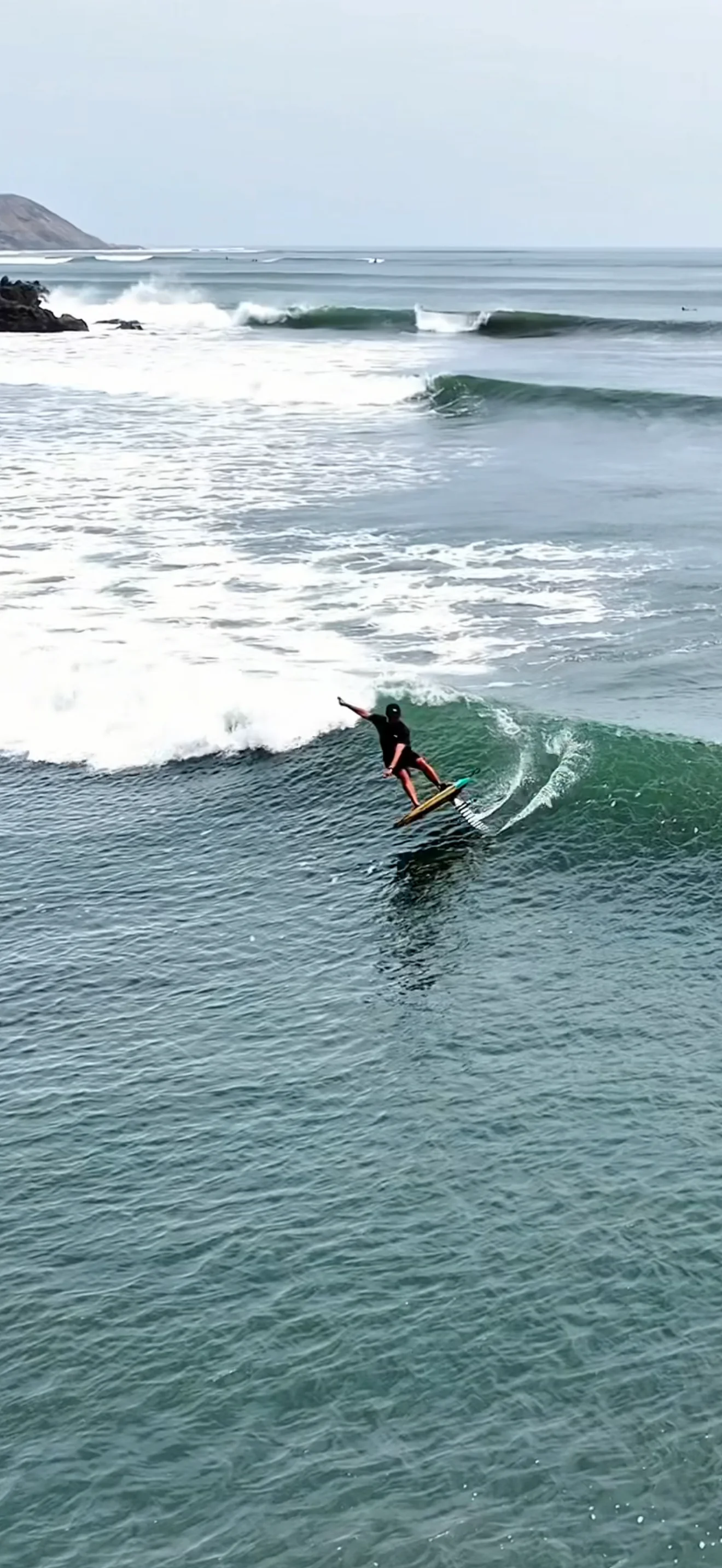 Paul Cooper foiling across a wave at Chicama with long wave lines behind him.