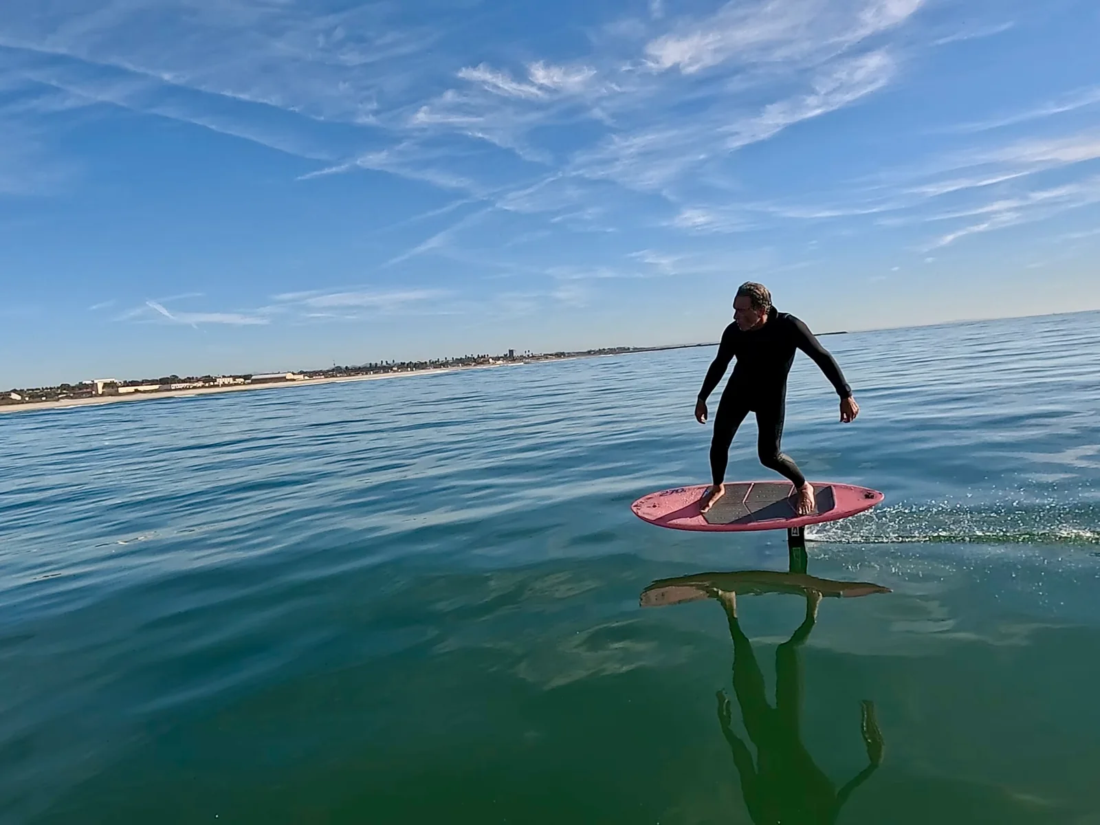 Ted Robinson riding a pink foil board above calm ocean water.