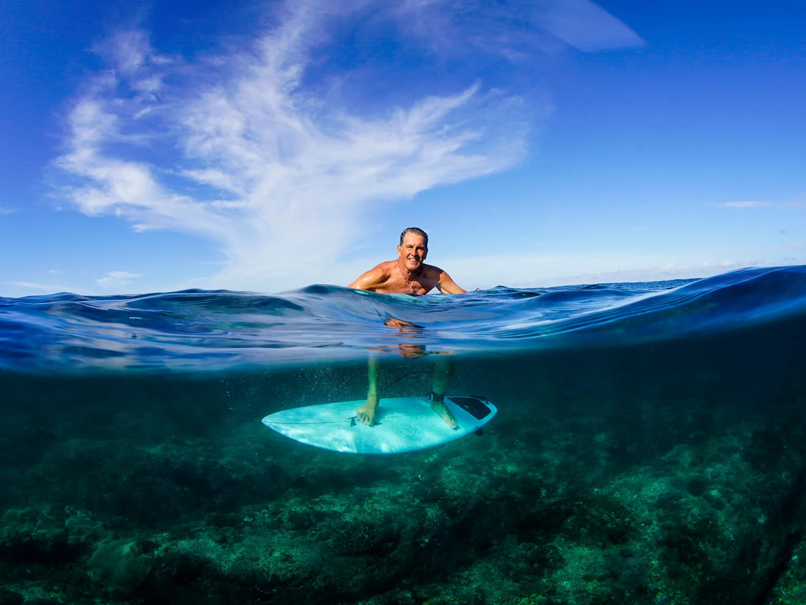 Ted Robinson smiling at water level with his surfboard visible below the ocean surface.